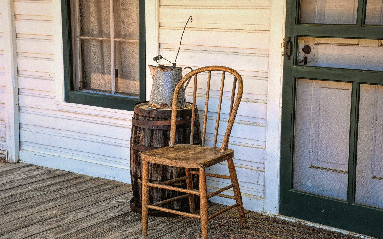A wooden chair and barrel with an old enamel pitcher on a porch